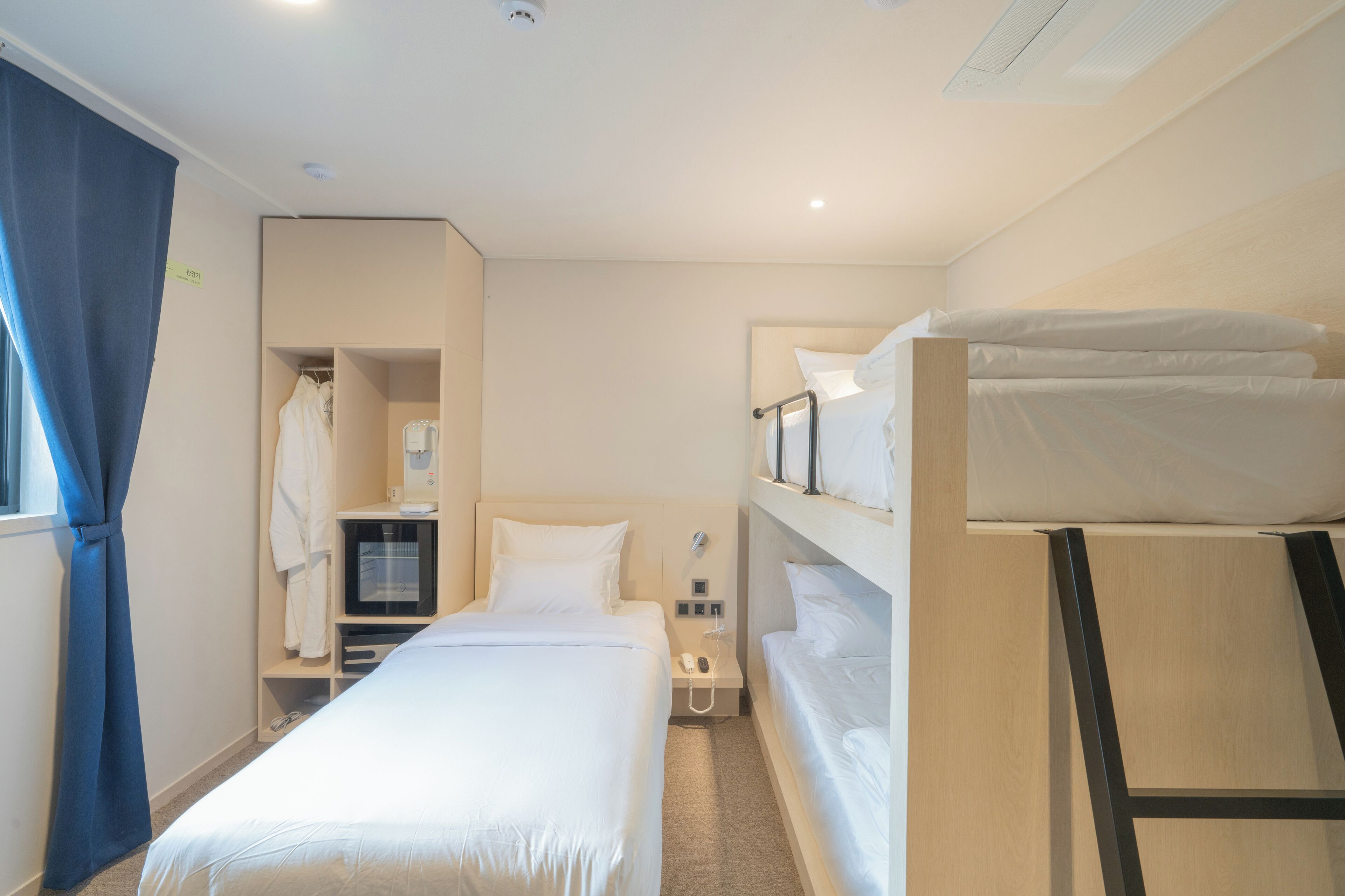 A hotel room with a single bed, a desk with a computer, a wardrobe, and a bunk bed.