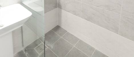 A modern bathroom with a glass shower enclosure, a white sink, and marble tiles.