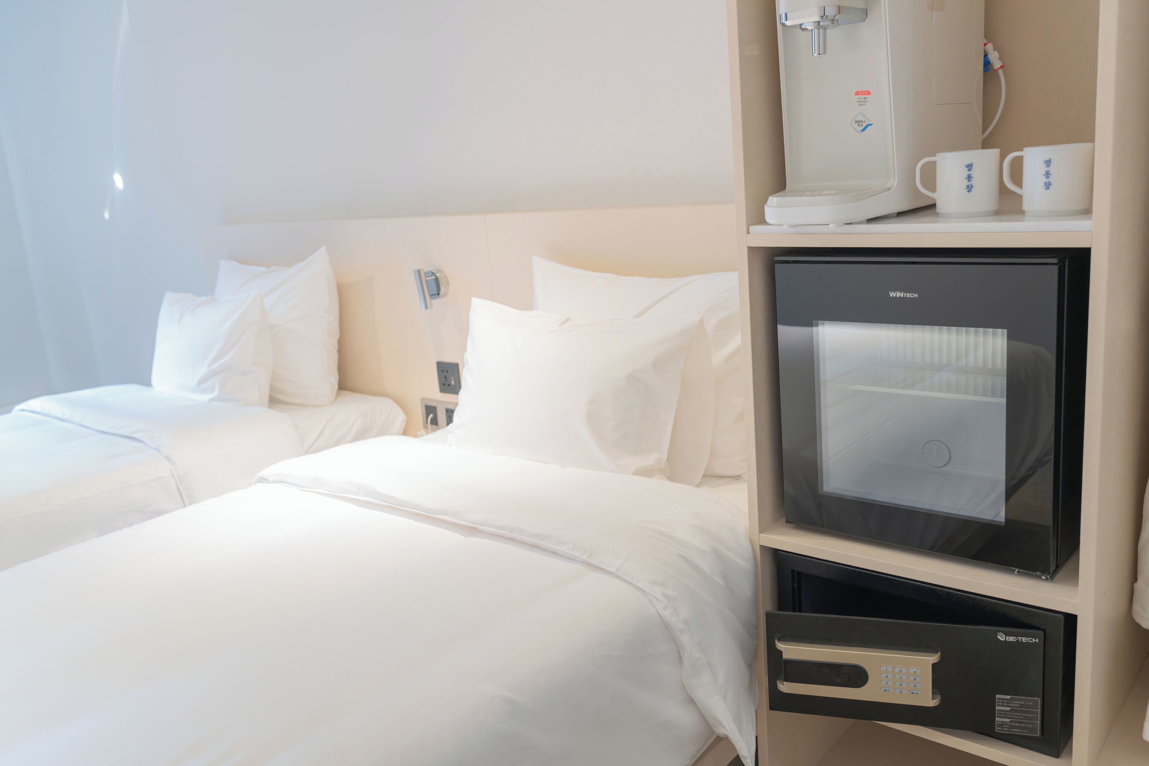 A hotel room with two beds, a minibar, a coffee machine, and a TV.
