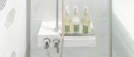 A shower with a chrome handle and a glass enclosure, a white tiled wall, and a shelf with three bottles of liquid soap.