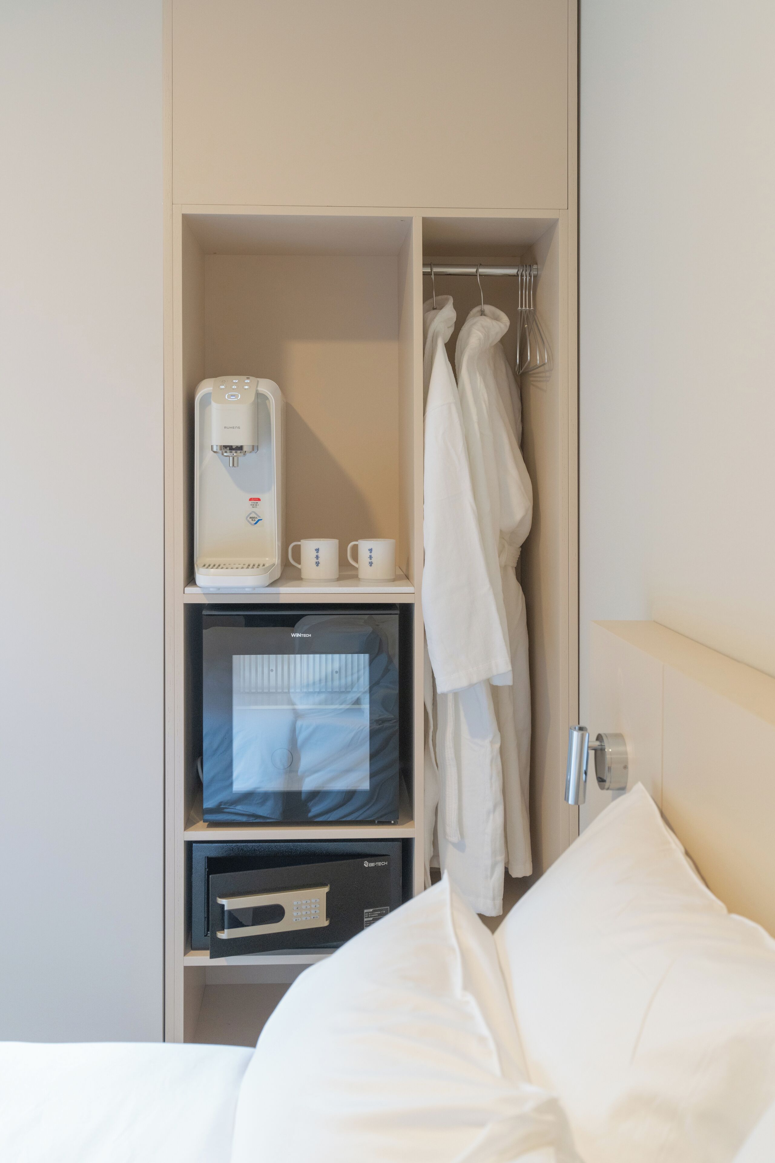 A hotel room with a minibar, a coffee machine, a microwave, and a hanging robe.