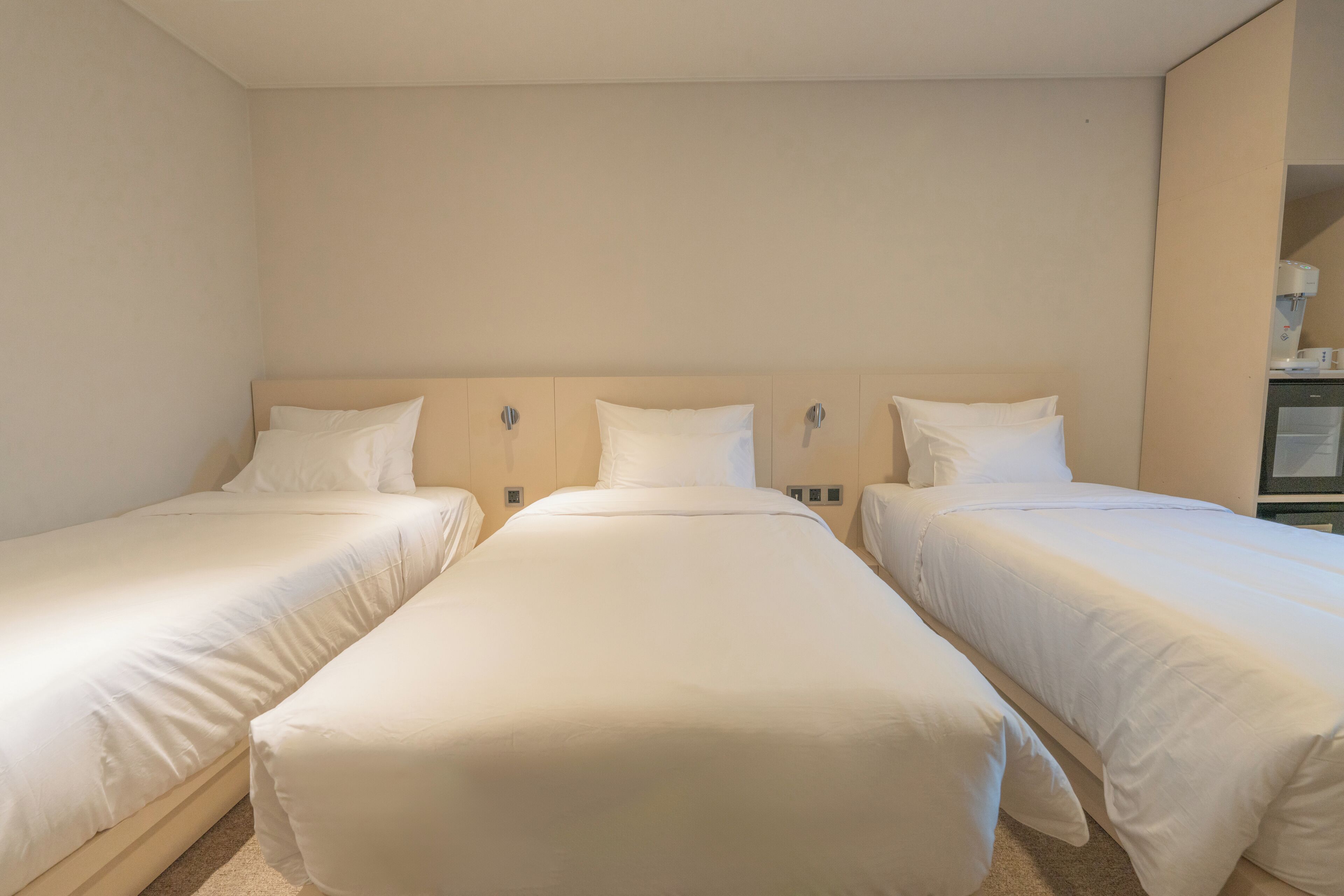 A hotel room with three single beds, a neutral color scheme, and a simple, clean design.