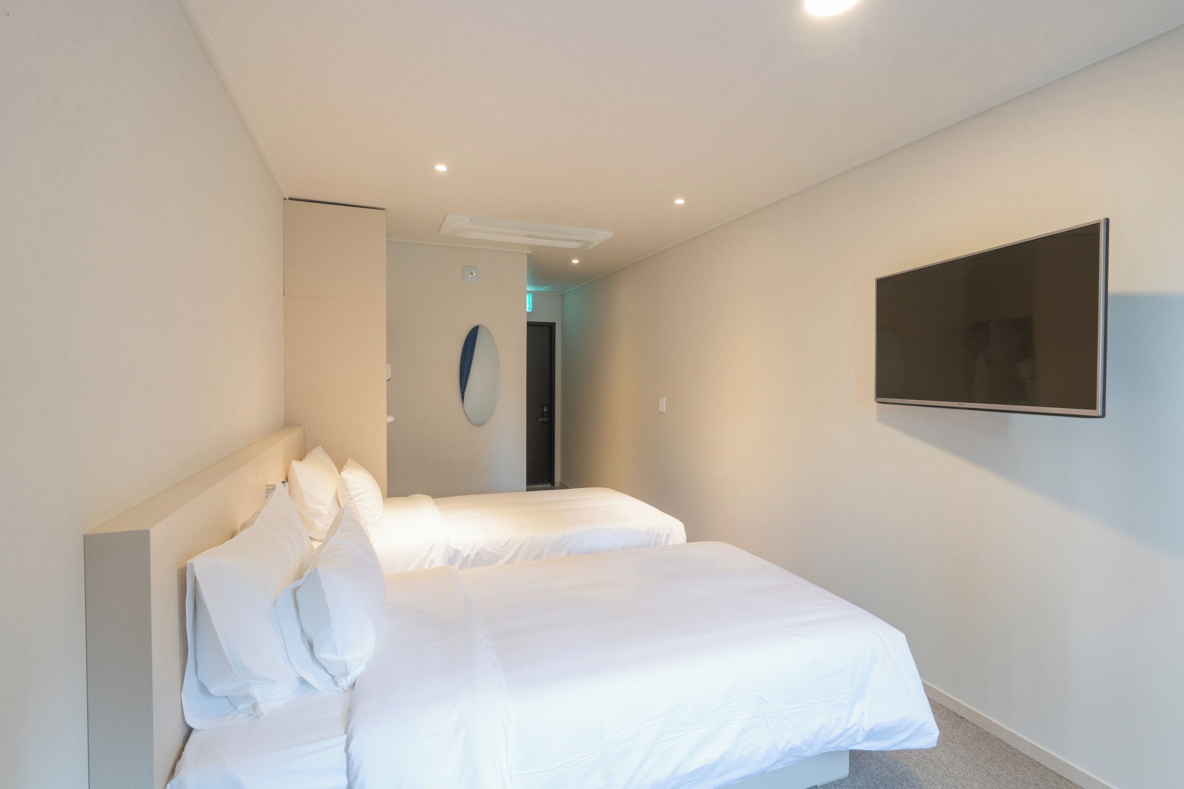 A hotel room with two beds, a flat-screen TV mounted on the wall, and a door leading to another room.