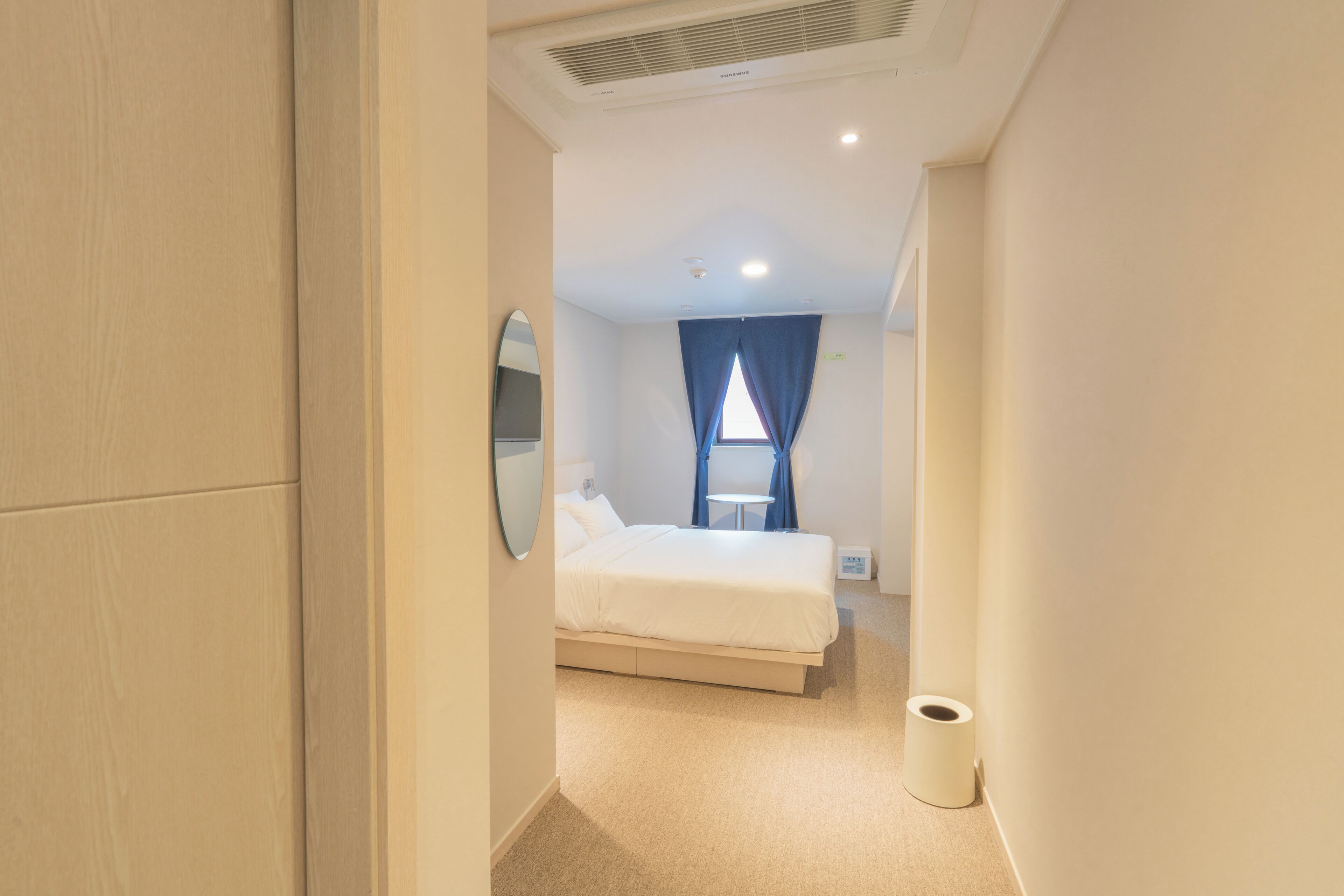 A hotel room with a bed, a bedside table, a mirror, and a window with curtains.