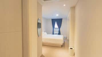 A hotel room with a bed, a bedside table, a mirror, and a window with curtains.