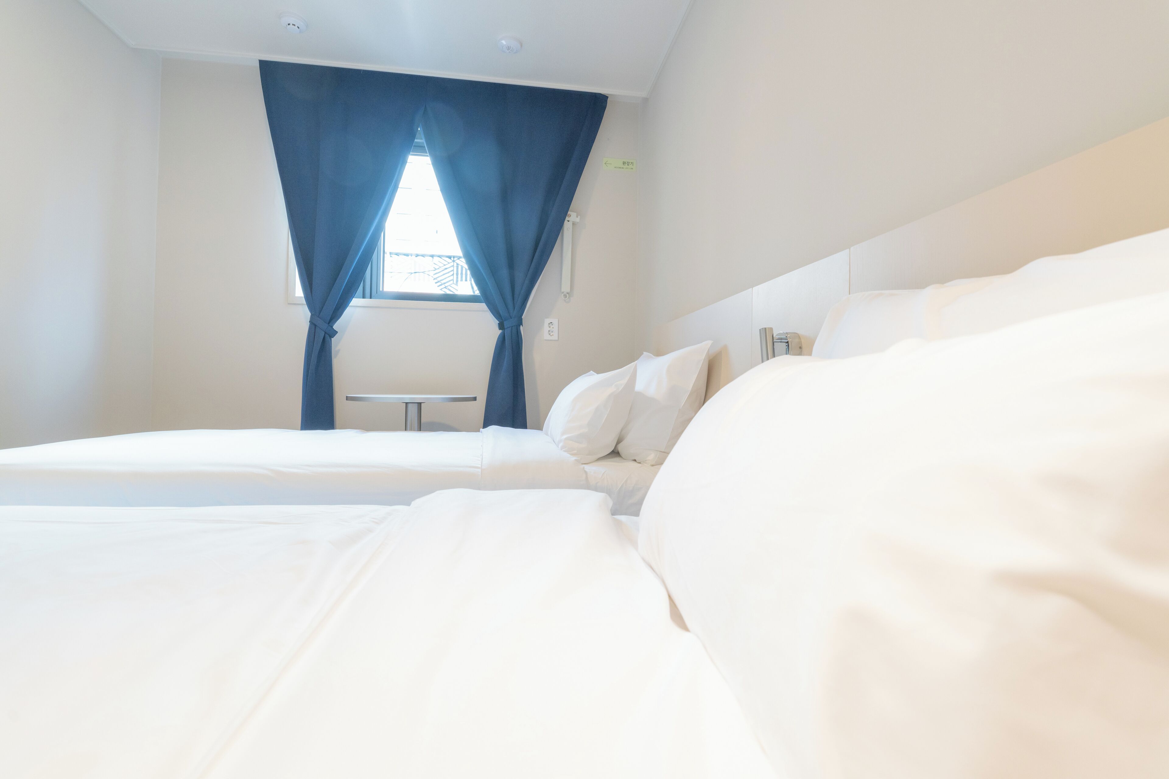 A hotel room with two beds, a window with blue curtains, and a small table.
