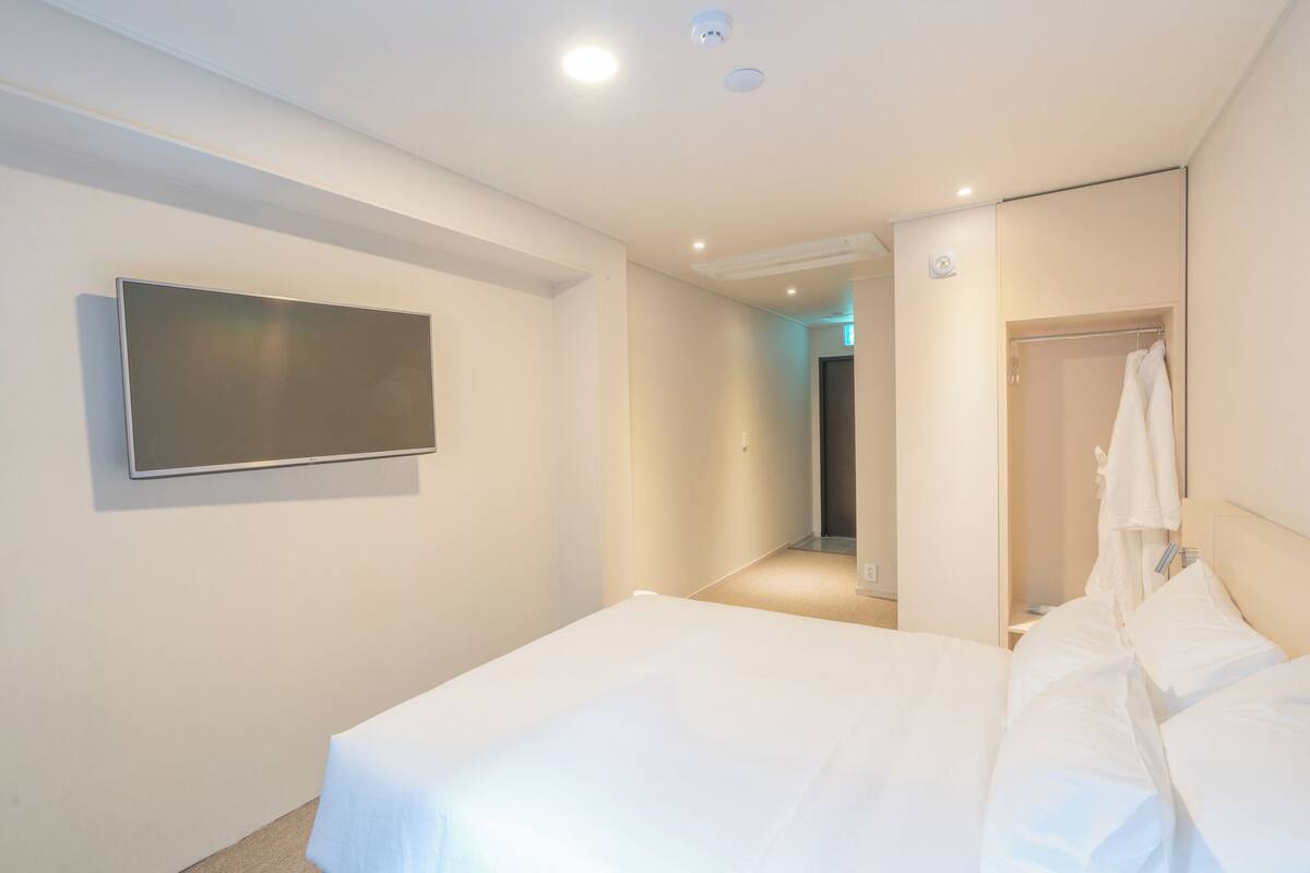 A modern hotel room with a large bed, a flat-screen TV mounted on the wall, and a walk-in closet.