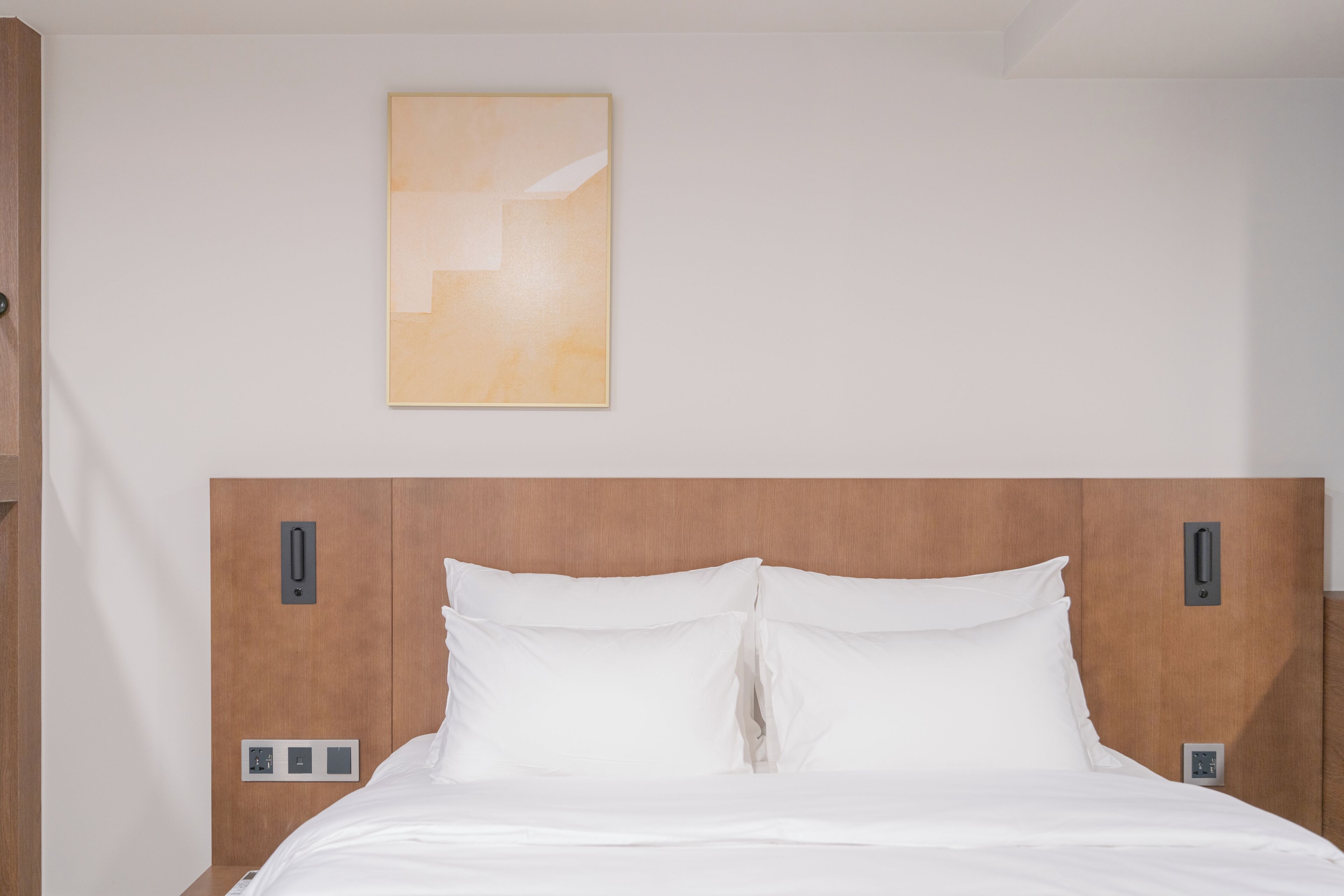 A hotel room with a wooden headboard, white bedding, and a wall-mounted artwork.