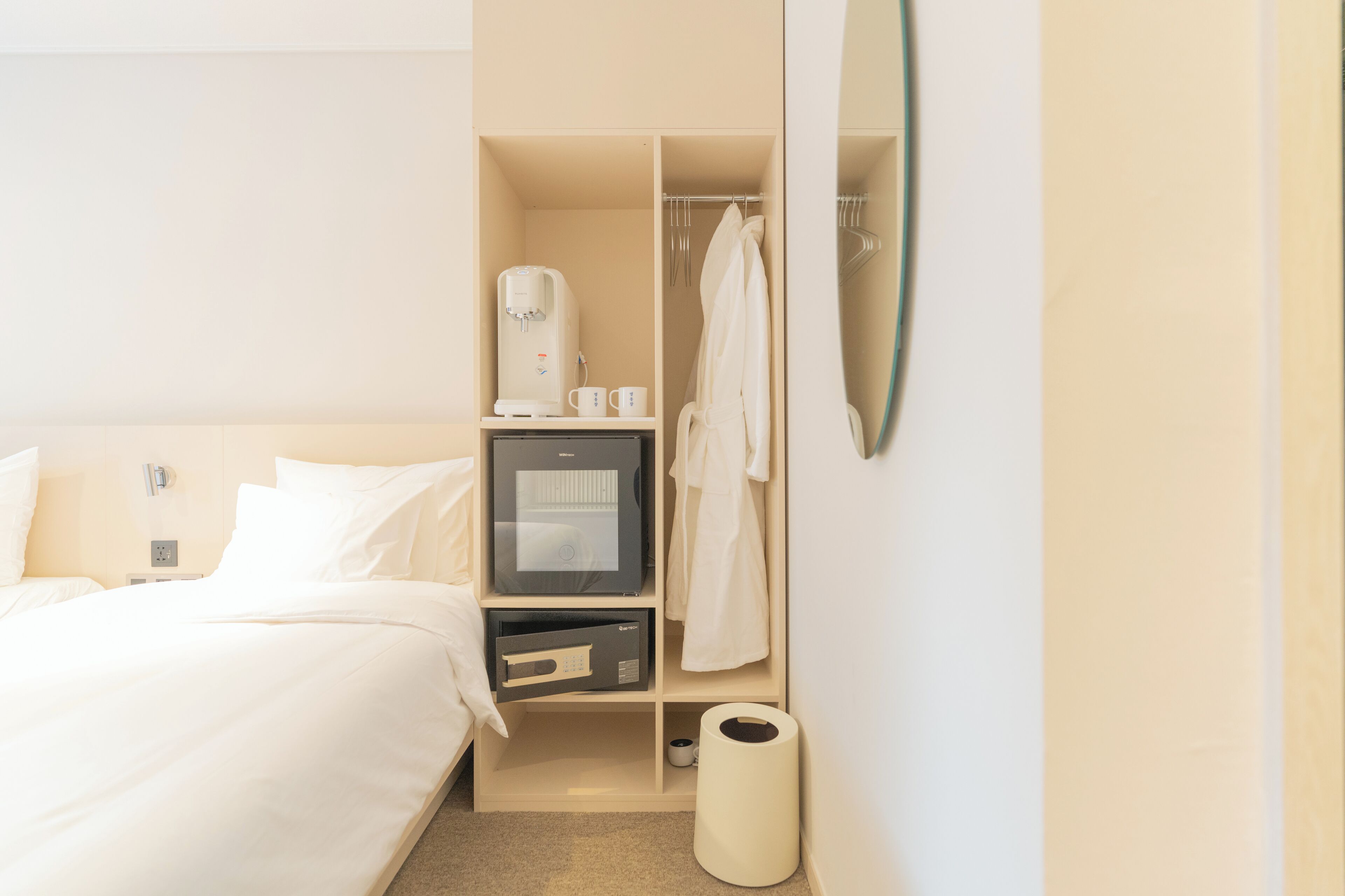 Quarto de hotel com cama, minibar, máquina de café, roupão e lixeira.
