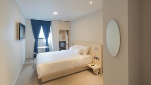 Moderni hotellihuone, jossa on suuri sänky, yöpöytä, jossa on puhelin, pieni työpöytä tuolilla, televisio ja peili seinällä.