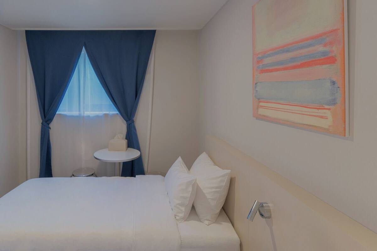 A hotel room with a bed, a small round table, and a painting on the wall.
