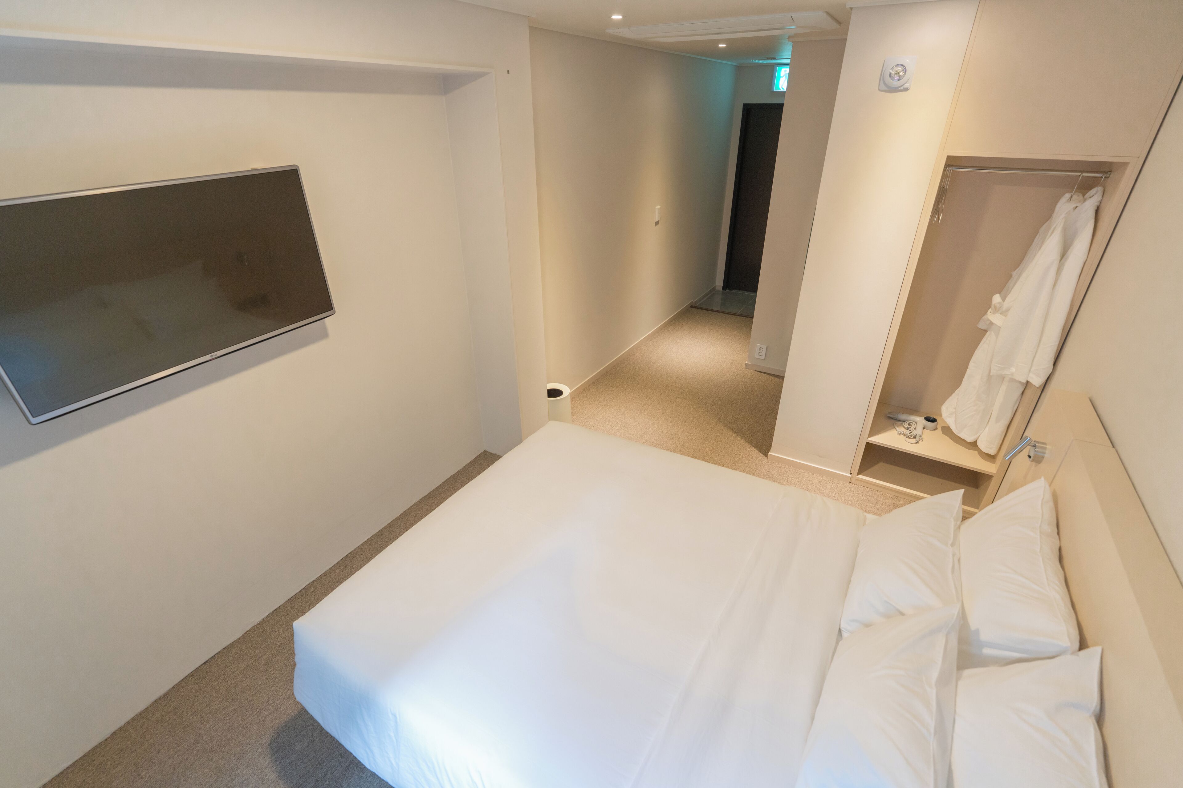 Ein Hotelzimmer mit Bett, Wandfernseher, Spiegel und Duschbereich.