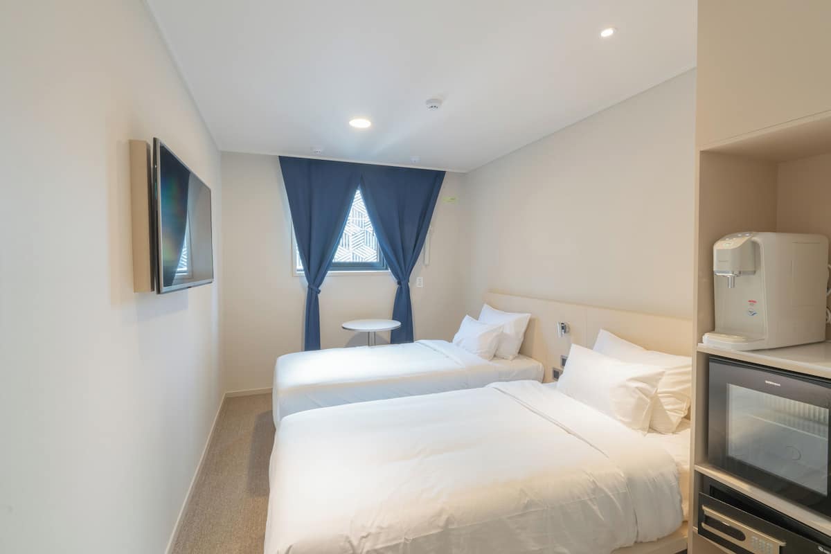 A hotel room with two beds, a small table, a TV, and a coffee machine.