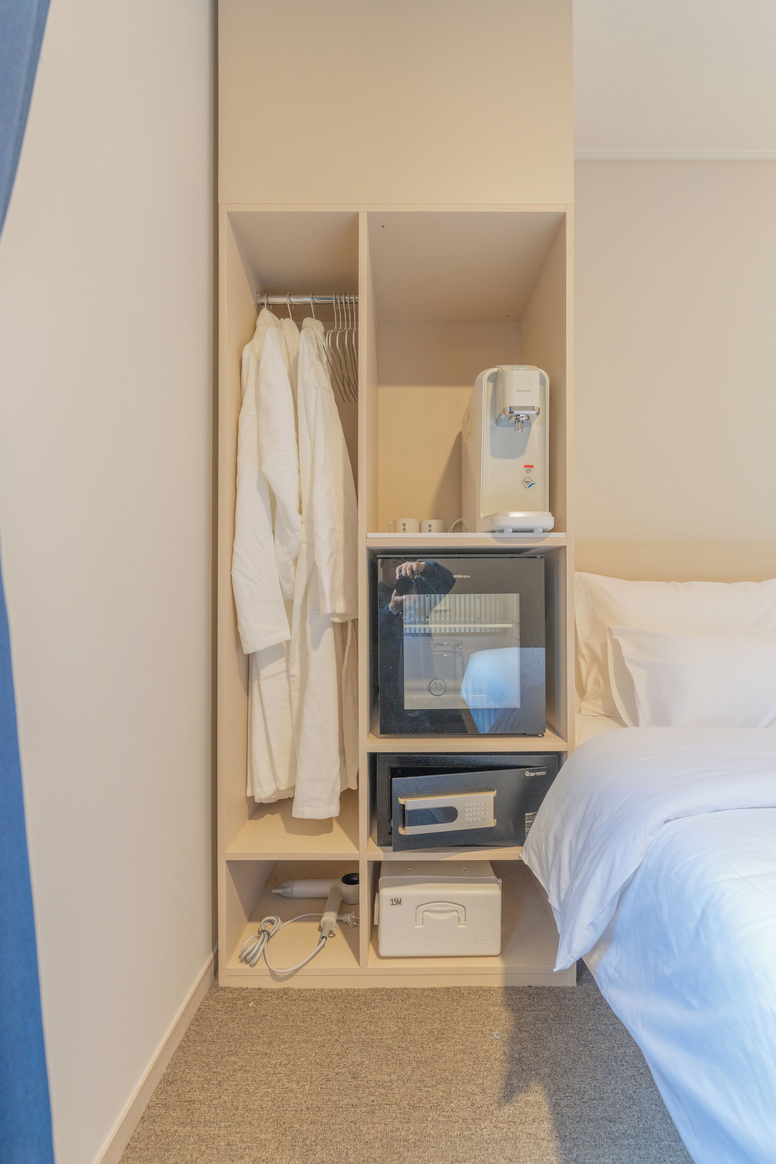 Una habitación de hotel con una cama, un estante con microondas, dispensador de agua y una bata colgada en un perchero.