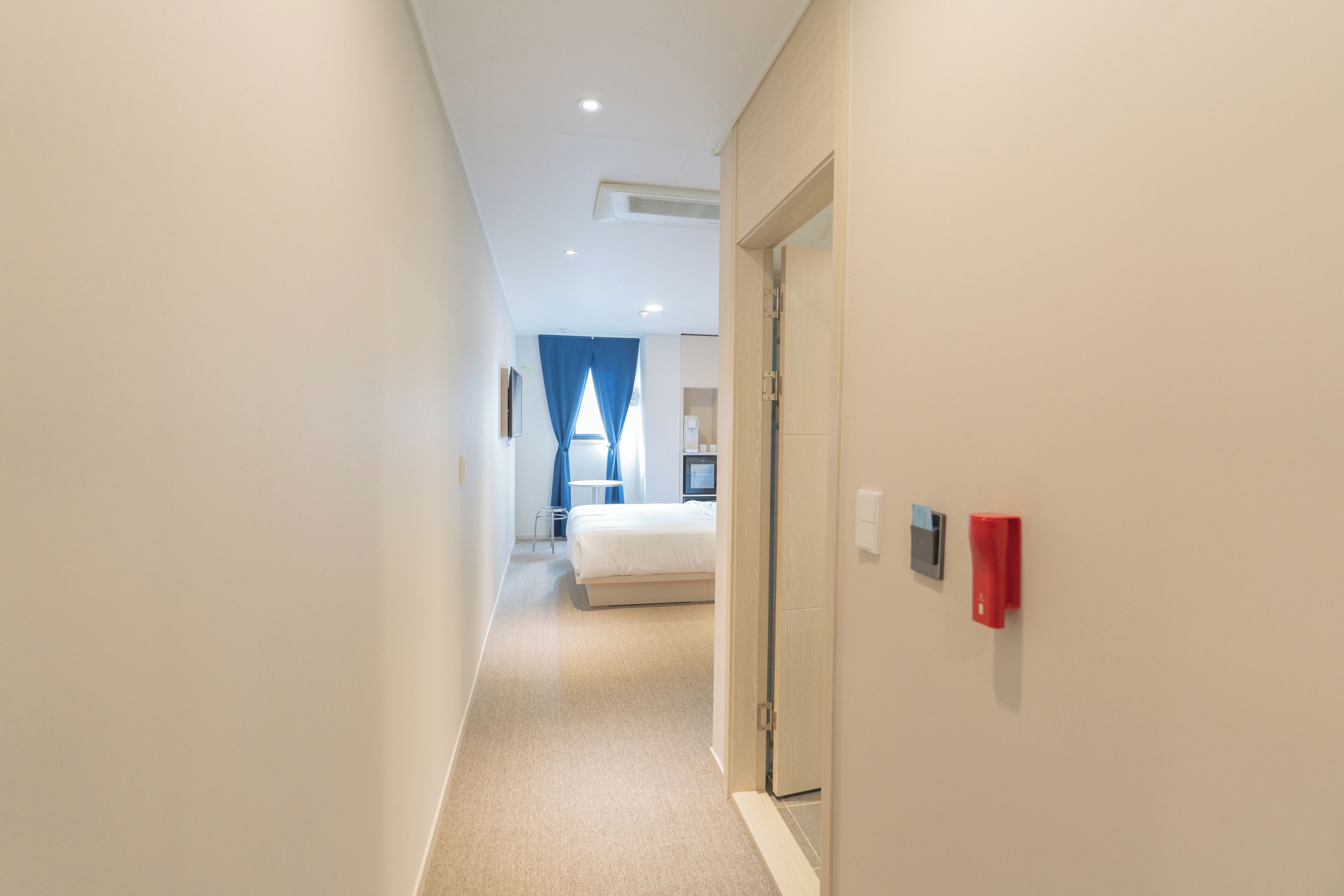 A hotel hallway with a bed, a desk, and a red object on the wall.