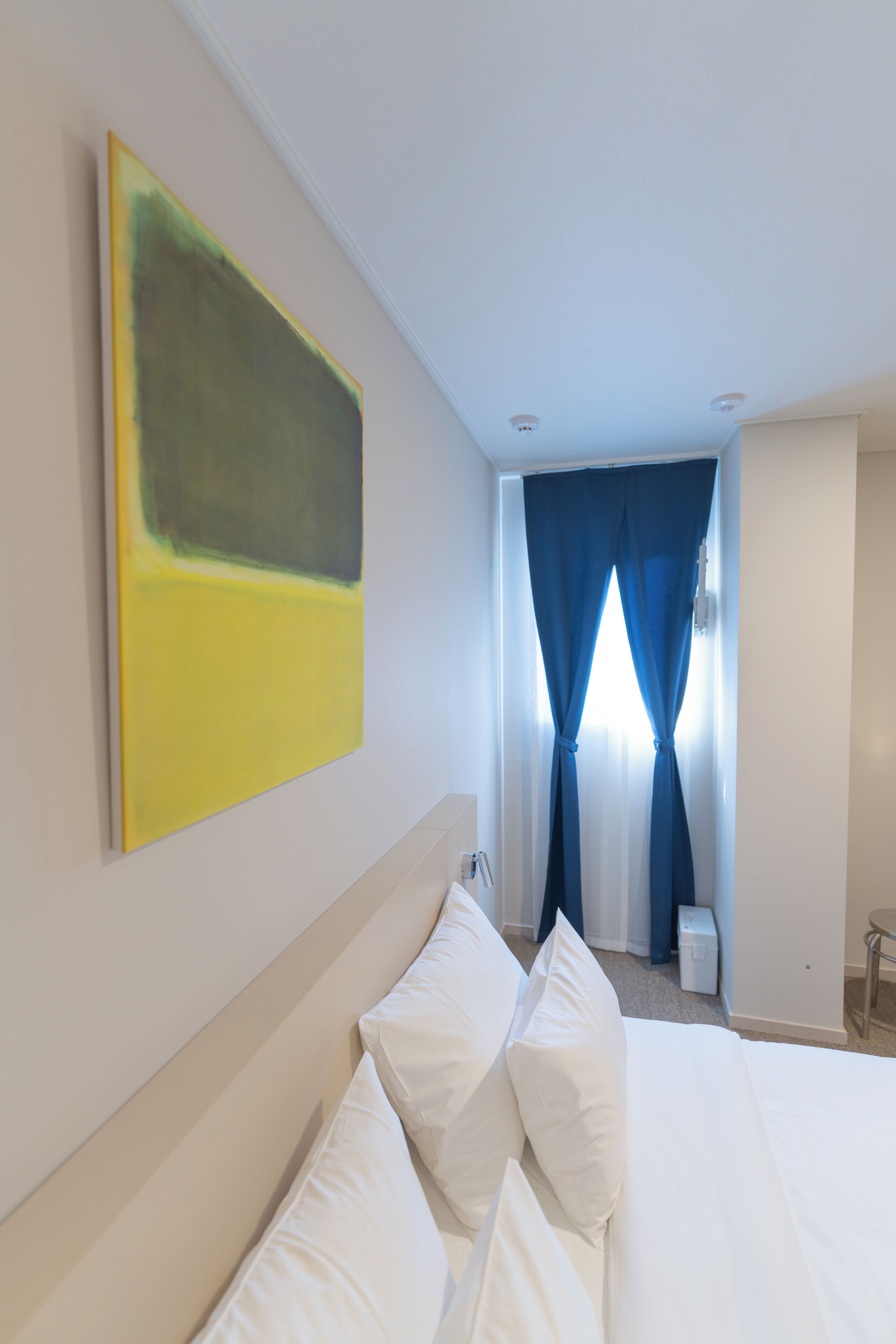 Une chambre d’hôtel avec un grand lit, un tableau au mur et une fenêtre avec des rideaux.