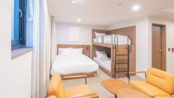 A hotel room with a bunk bed, a single bed, a wooden table, and two yellow chairs.