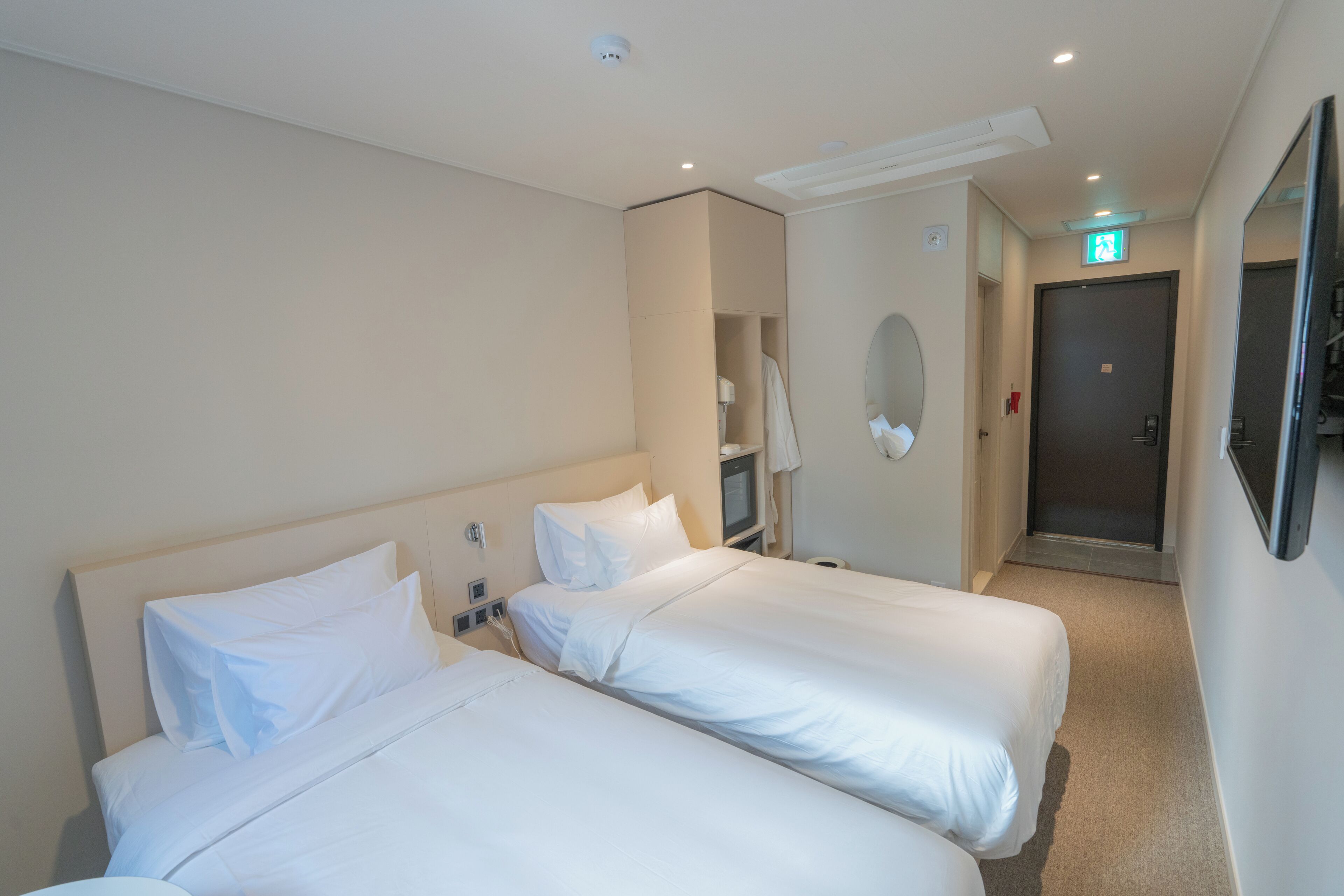A hotel room with two beds, a mirror, a wardrobe, and a door leading to a bathroom.