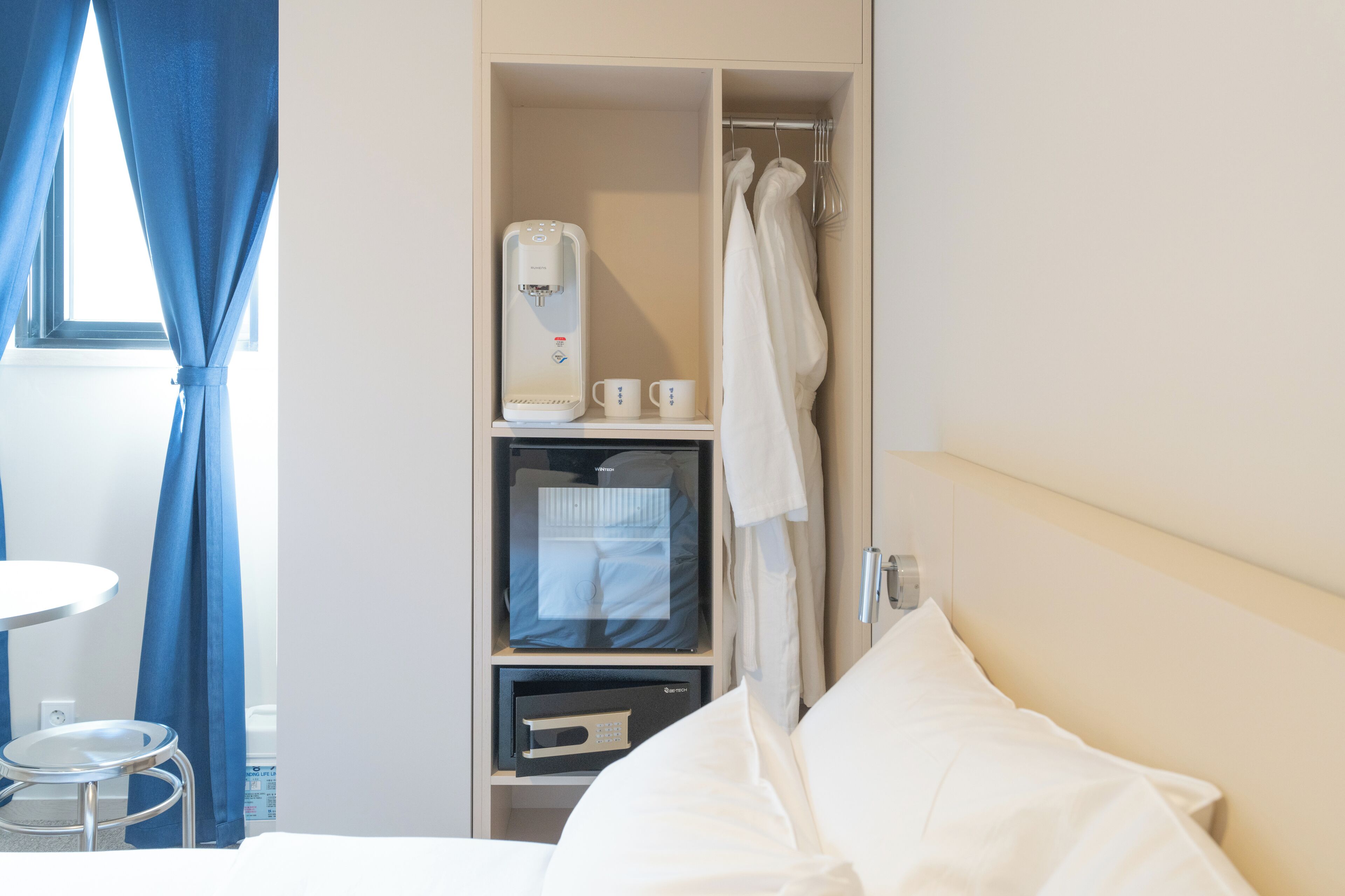 A hotel room with a bed, a small table, a coffee machine, and a shower area.