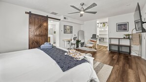 A bedroom with a large bed, a ceiling fan, a wooden door, a desk, a chair, a mirror, and a TV. - Space Cowboy Retreat • Sleeps 11 • Fire Pit • Near NRG (Houston)