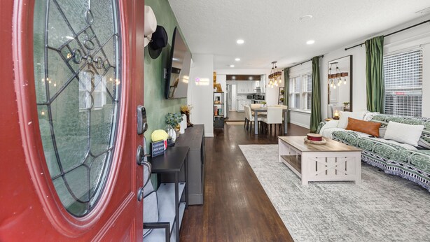 A modern living room with a dining area, a kitchen in the background, and a red door with a glass window. - Space Cowboy Retreat • Sleeps 11 • Fire Pit • Near NRG (Houston)