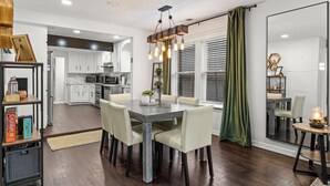A modern kitchen with white cabinets, a dining area with a wooden table and chairs, and a large mirror reflecting the room. - Space Cowboy Retreat • Sleeps 11 • Fire Pit • Near NRG (Houston)