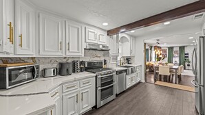 A modern kitchen with white cabinetry, stainless steel appliances, and a wooden ceiling beam. - Space Cowboy Retreat • Sleeps 11 • Fire Pit • Near NRG (Houston)