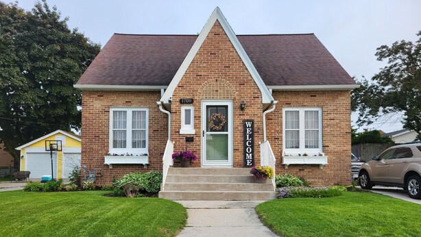 A two-story brick house with a welcoming sign, a front door, and a garage.