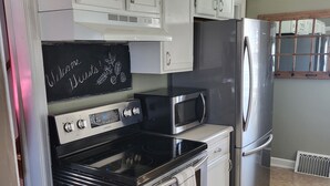 A kitchen with white cabinets, a stainless steel refrigerator, a microwave, a stove, and a chalkboard with 'Welcome Guests!' written on it.