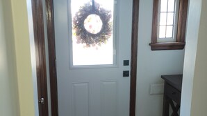 A white door with a wreath, a small window, and a dark wooden bench.