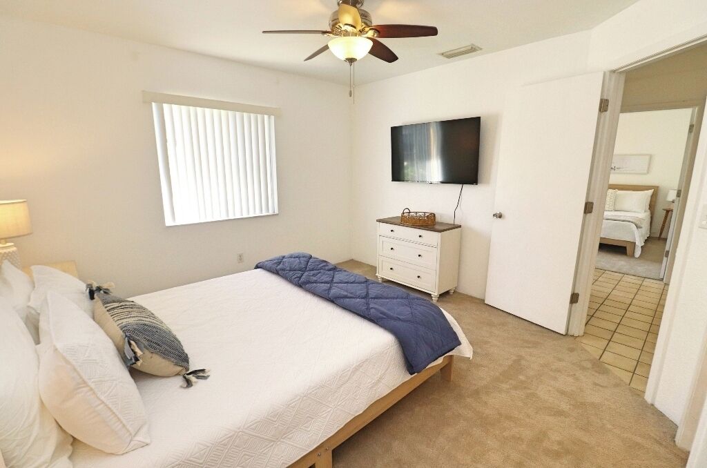 A bedroom with a bed, a ceiling fan, a TV, a dresser, and a window with blinds.
