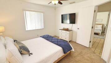 A bedroom with a bed, a ceiling fan, a TV, a dresser, and a window with blinds.