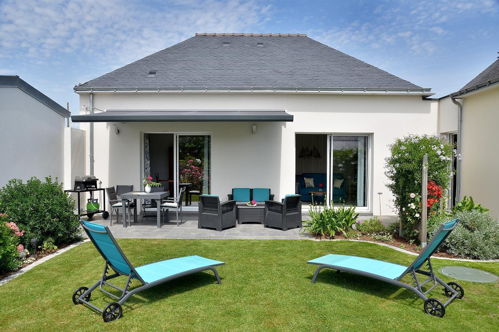 Ein modernes Haus mit Terrasse, Gartenmöbeln und Rasenfläche.