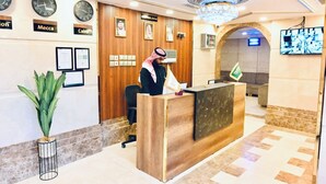 A hotel reception area with a wooden reception desk, multiple clocks, framed certificates, and a chandelier. - Golden Hospitality Hotel (Makkah)