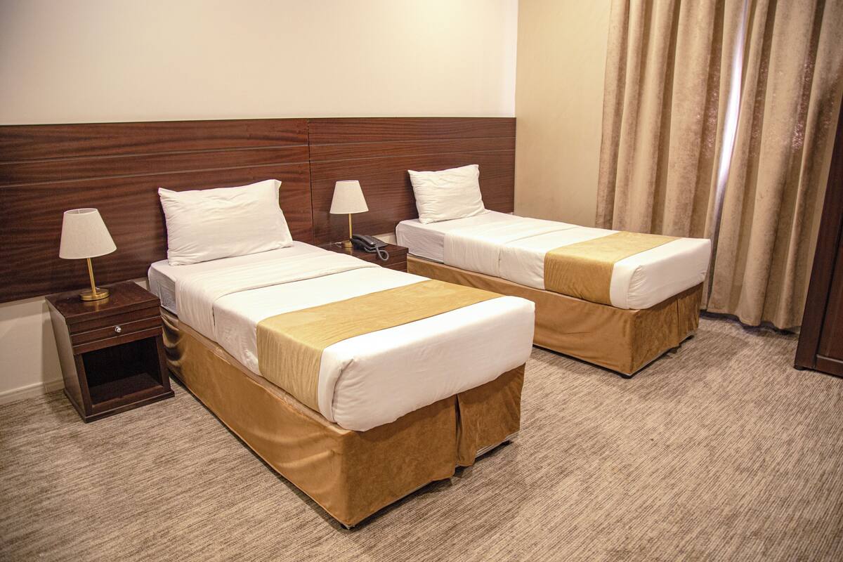 A hotel room with two beds, each with a wooden headboard, a bedside table with a lamp, and a carpeted floor.