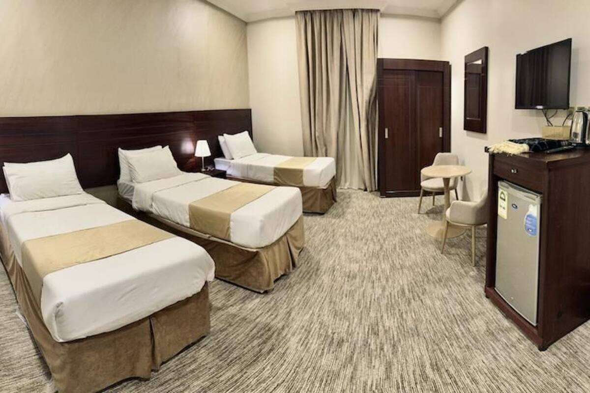 A hotel room with two beds, a desk, a chair, a television, and a minibar.