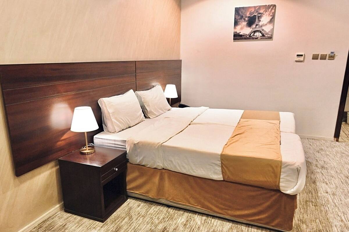 A hotel room with a large bed, a nightstand with a lamp, a headboard, and a picture of the Eiffel Tower on the wall.