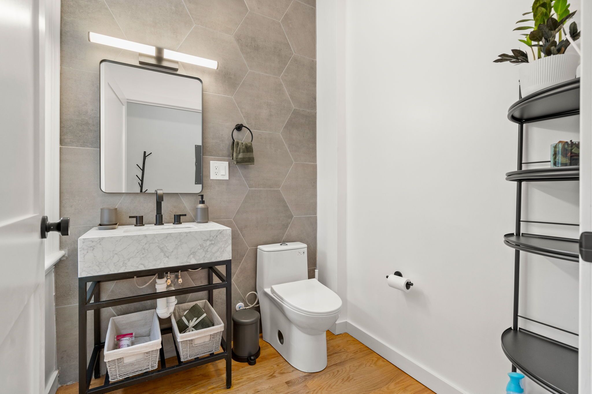 Een moderne badkamer met een marmeren wastafel, toilet en een zwarte metalen schapunit met een plant.