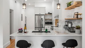Uma cozinha moderna com armários brancos, eletrodomésticos de aço inoxidável e iluminação pendente.