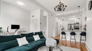 Sala de estar moderna com sofá verde, uma mesa de centro de vidro e uma cozinha ao fundo.