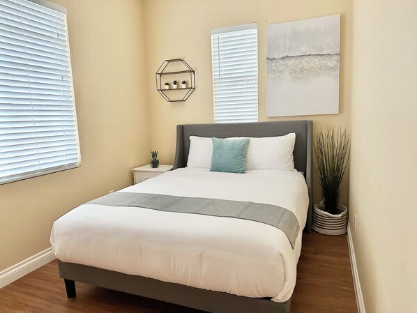 Um quarto com cama, mesas de cabeceira, uma planta em vaso e obras de arte nas paredes.