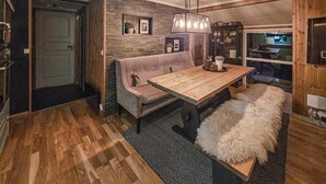 A cozy dining area with a wooden table and bench, a cushioned bench seat, a hanging light fixture, and a rustic brick wall. - 3 bedroom nice home in Tuddal (Tuddal)