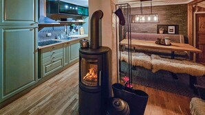 A cozy living room with a wood-burning stove, a dining area with a table and chairs, and a kitchen with cabinets and a stove. - 3 bedroom nice home in Tuddal (Tuddal)