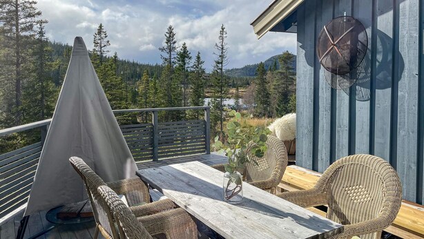 A wooden deck with wicker furniture, a table, and chairs, overlooking a forested valley. - 3 bedroom nice home in Tuddal (Tuddal)