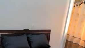 Un letto con una testiera scura, due cuscini, un piccolo tappeto e una tenda parzialmente visibile.