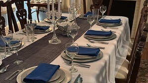 Ein eleganter Speisesaal mit einem langen Tisch, gedeckt für eine Mahlzeit, mit weißen Tischdecken, blauen Servietten und Besteck.