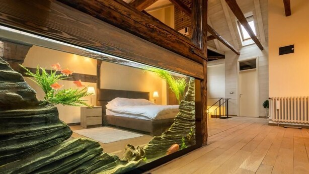 A bedroom with a bed, bedside tables, and a large window overlooking a living area.