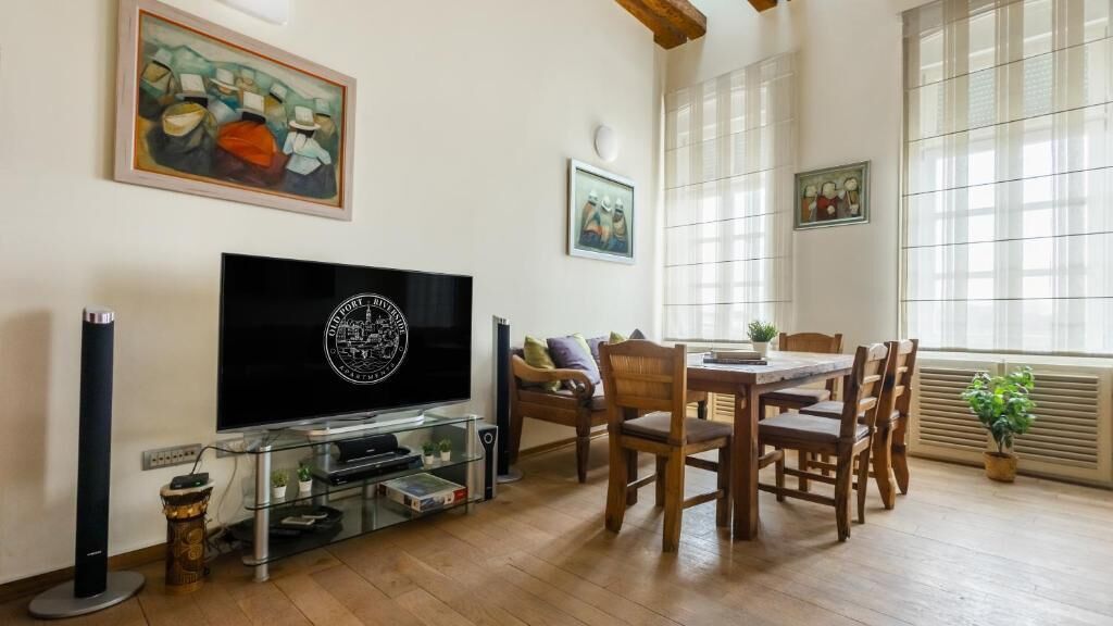 A living room with a flat-screen TV, wooden dining table, chairs, and artwork on the walls.