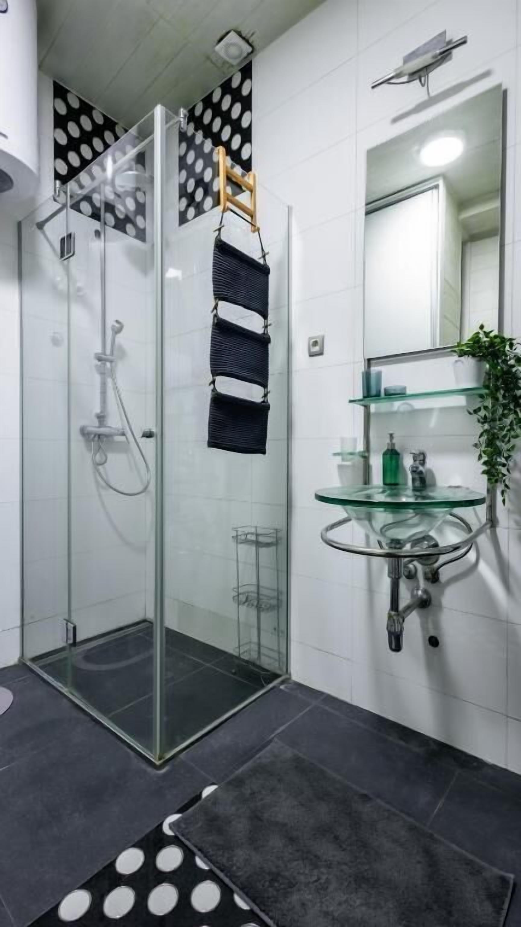 A modern bathroom with a glass shower enclosure, a glass sink with a mirror, and a black and white polka dot shower curtain.