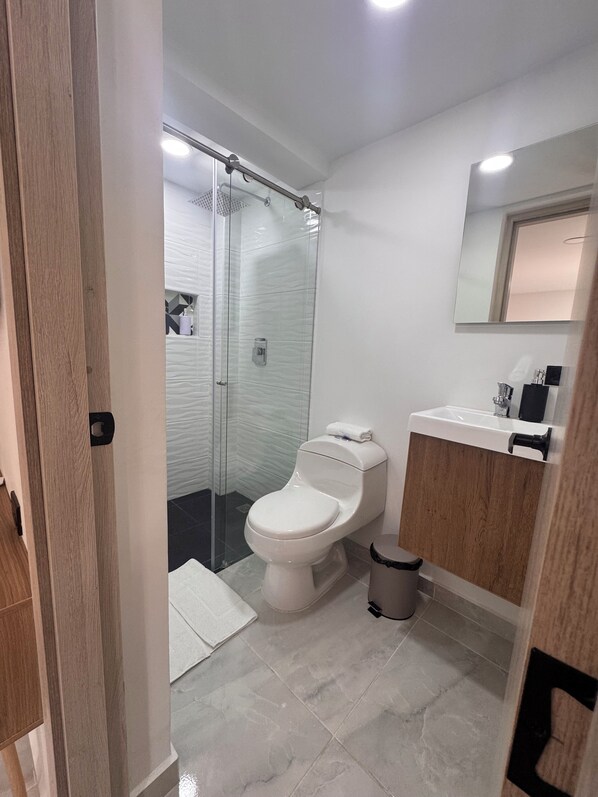 A modern bathroom with a glass-enclosed shower, a white toilet, and a wooden vanity with a mirror. - Vida Hostel (Medellín)